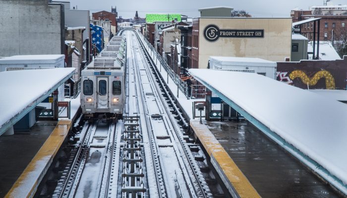 A subway train is departing from a snow-covered above ground platform.