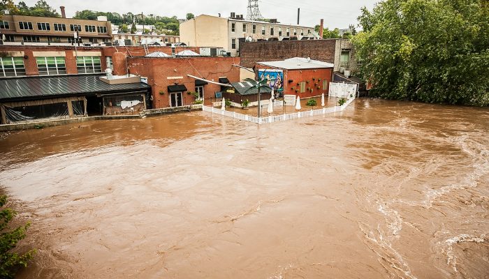 Brown, muddy floodwater from Schyulkill River with buildings in Manyunk adjacent to the river in the background.