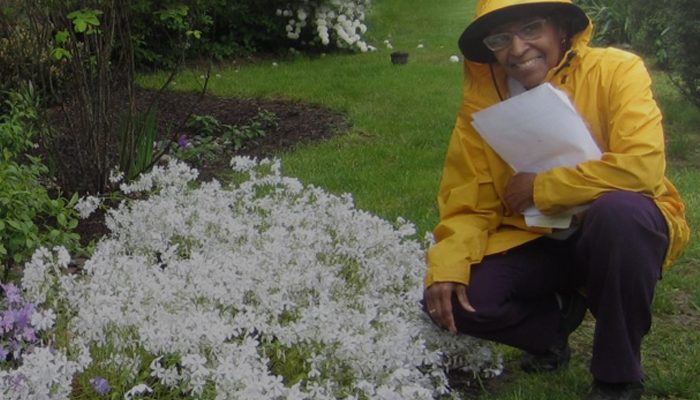 A woman in a raincoat kneels near flowers.