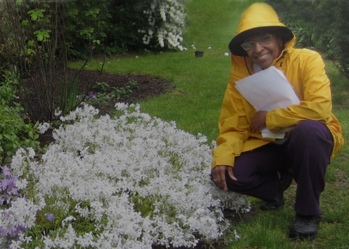 A woman in a raincoat kneels near flowers.