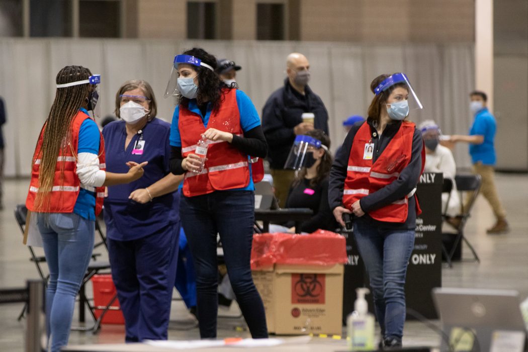Nurses and other medical personnel wear plastic face shields as well as heavy duty surgical masks as they talk at a Philadelphia COVID-19 vaccine clinic at the Pennsylvania Convention Center.