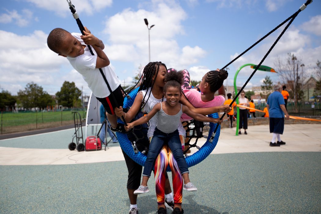 Four children play together on a playground swing set.