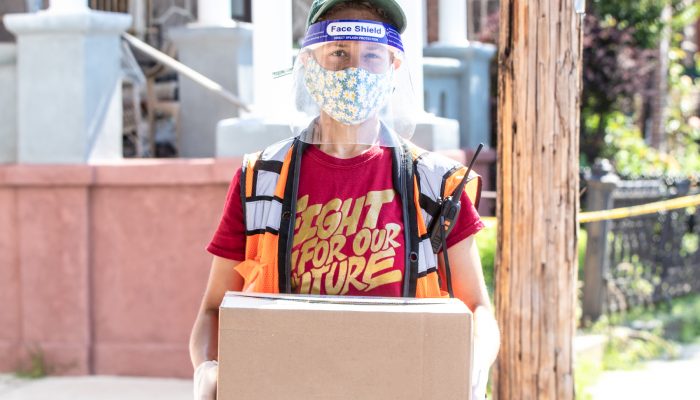 person with a face shield and mask holding a box of food for families