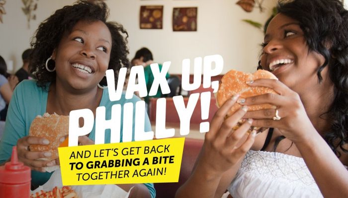 two people smiling and eating burgers with the text, Vax Up, Philly and let's get back to grabbing a bite together again