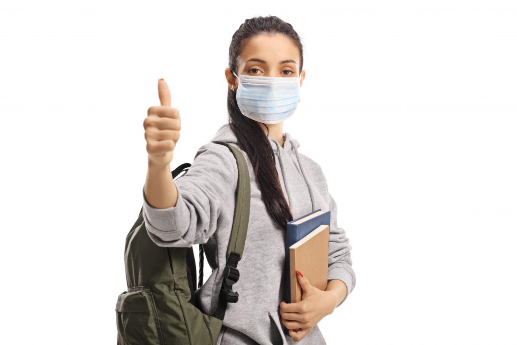 Female student with a medical face mask showing thumbs up isolated on white background