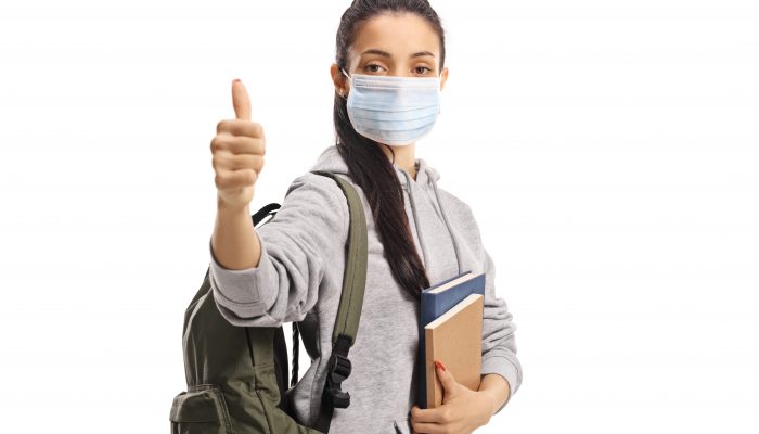 Female student with a medical face mask showing thumbs up isolated on white background