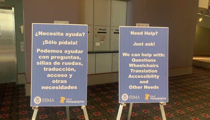 Signs in English and Spanish that direct people to ask for help with questions, wheelchairs, translation, accessibility, and other needs