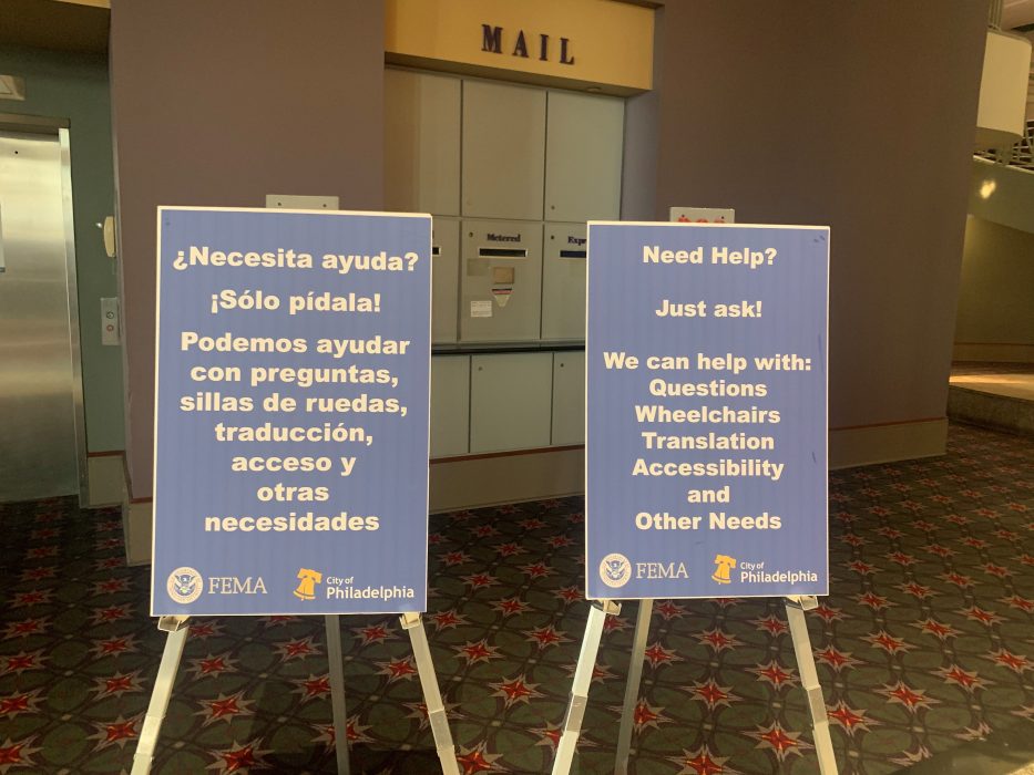 Signs in English and Spanish that direct people to ask for help with questions, wheelchairs, translation, accessibility, and other needs