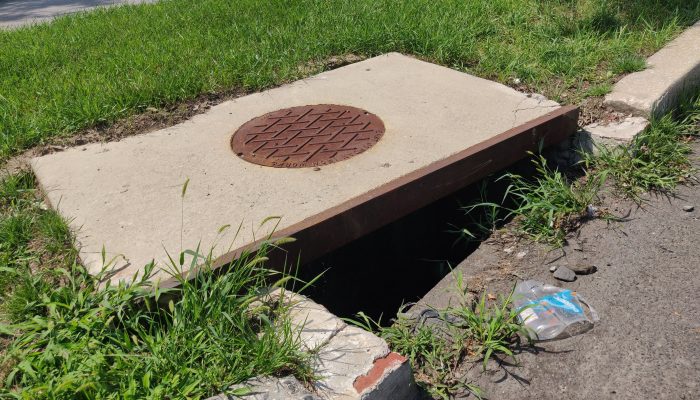 A cover for a storm drain is damaged and not aligned correctly, creating a hazard