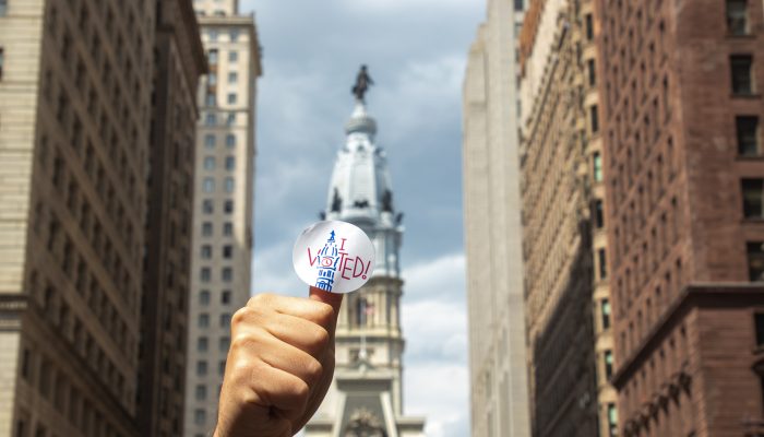 person with an i voted sticker on their thumb in front on city hall