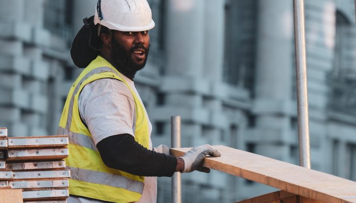 unmasked construction worker in helmet lifts piece of lumber