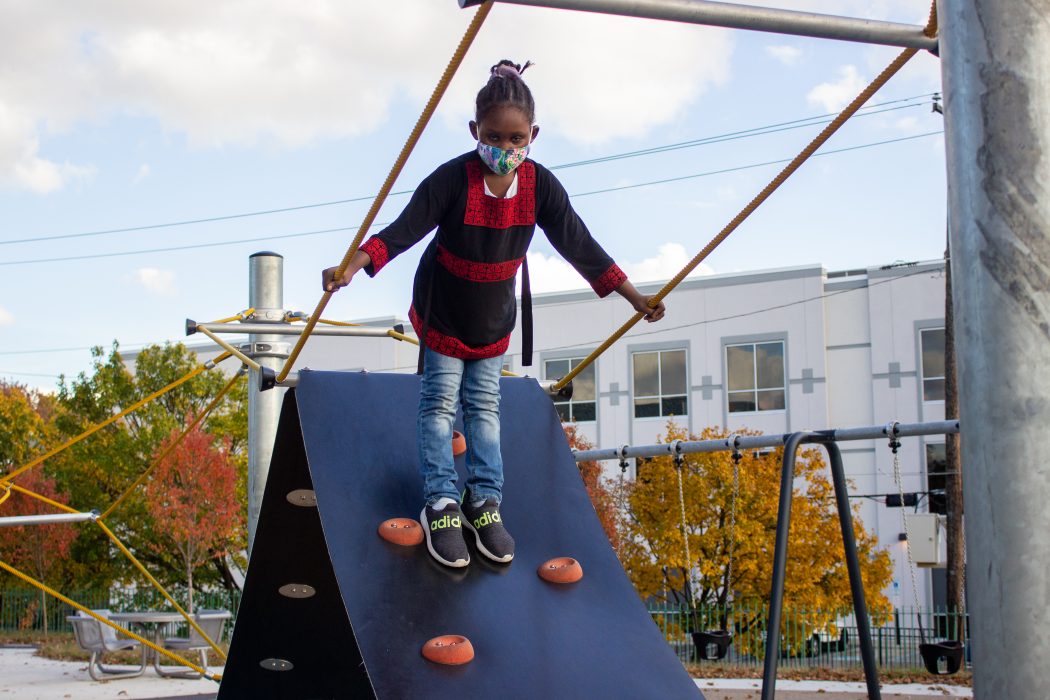 A girl wearing a face mask is standing at the top of a playground structure at a Rebuild site