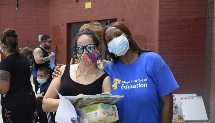 A community school coordinator and school community member pose together outside of a school building. 