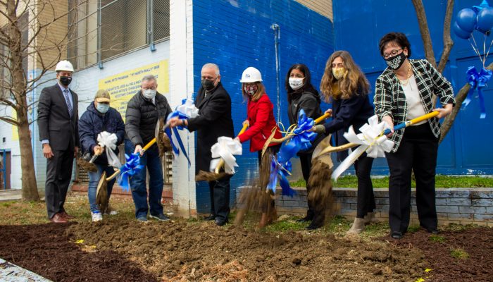City and community leaders, participating in a ceremony, shovel dirt from the ground in front of a community facility