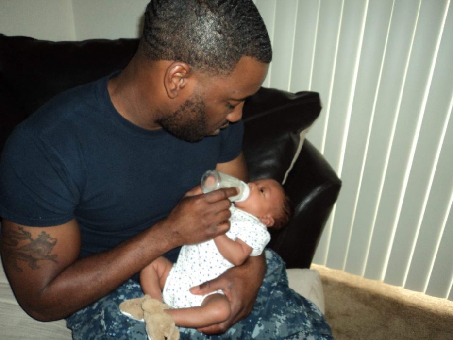Dad, Branden Kelly, holds his child in his arms. He is feeding the child with a bottle.