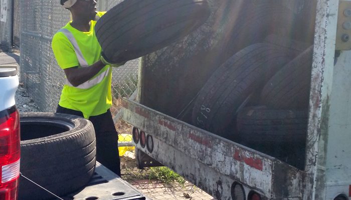Мужчина засовывает шину в кузов мусоровоза