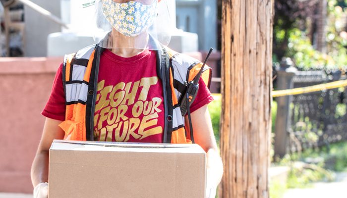 A worker wearing a face mask, face shield, orange vest, and a shirt that says 