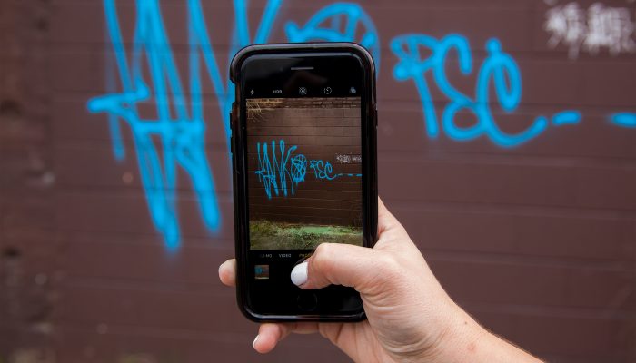 A hand holding a phone taking a picture of graffiti for a Philly311 service request