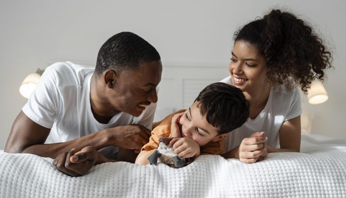 A happy Black family laughing while laying on a bed