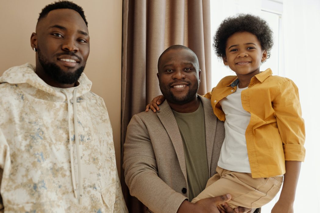 Image of two smiling black men, one of whom is holding a smiling child