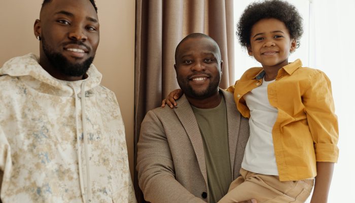 Image of two smiling black men, one of whom is holding a smiling child