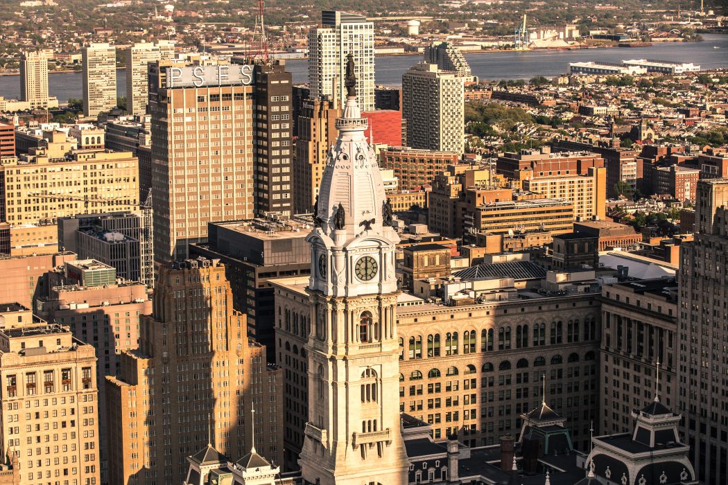 Philadelphia skyline during the day. Sunlight falls onto the buildings. City Hall stands at the forefront.