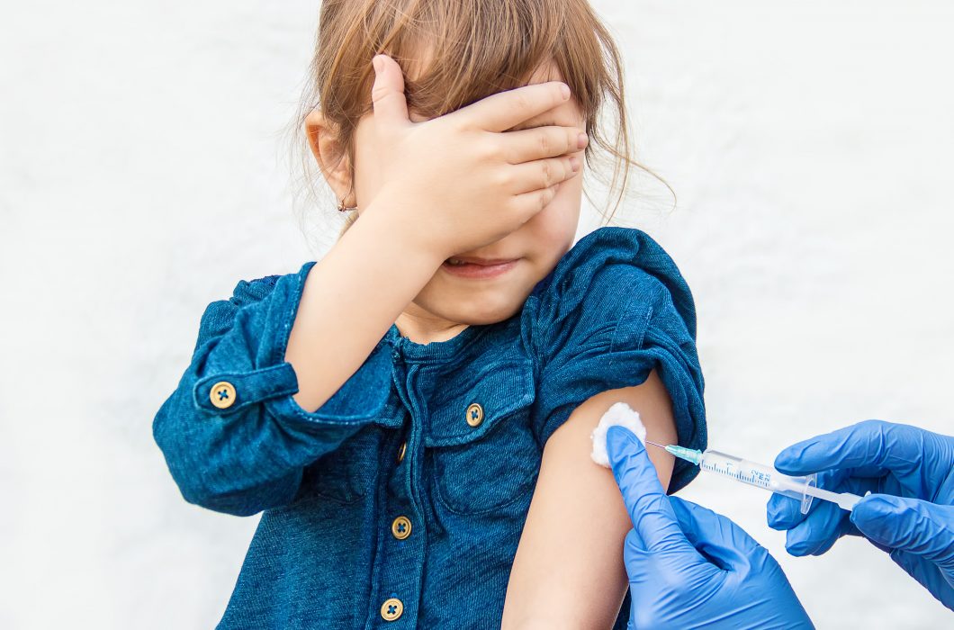 Child covering her eyes as she receives a vaccine
