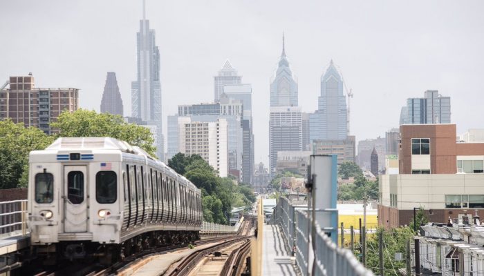 A Septa train is on the tracks leaving Philadelpha. The Philadelphia skyline is in the background.