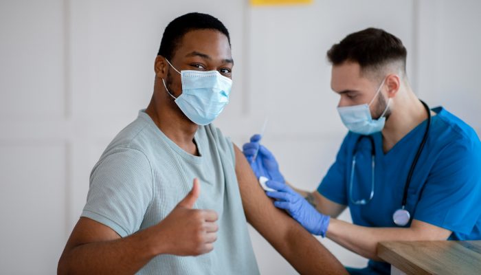 African American man wearing a face mask giving a thumbs up while being vaccinated