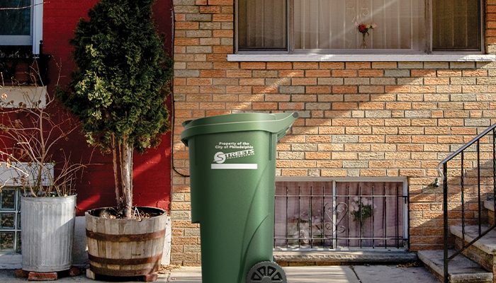 Uma lixeira verde Philacan na calçada em frente a uma casa