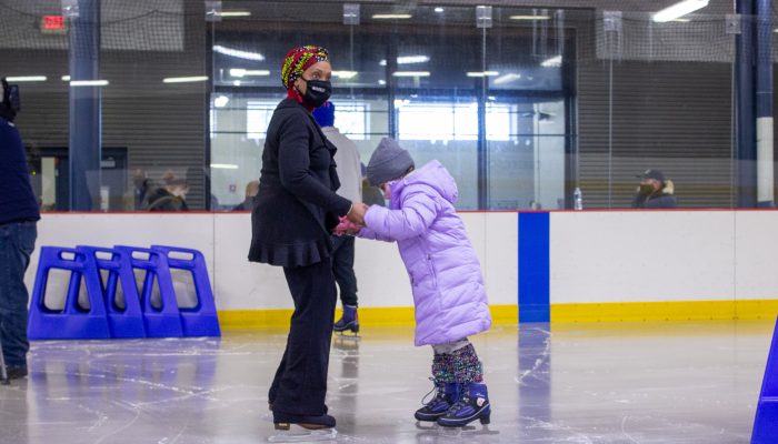Ice skating instructor guides child on ice rink