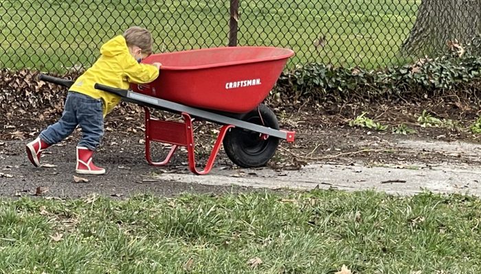 A small child pushing a red wheelbarrow