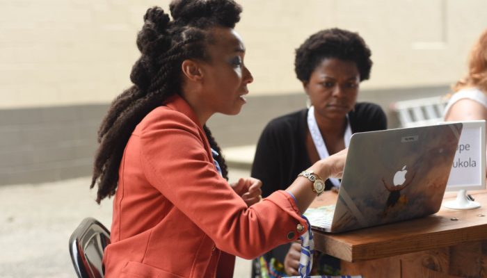 A woman is pointing to a laptop and talking to the woman sitting next to her.