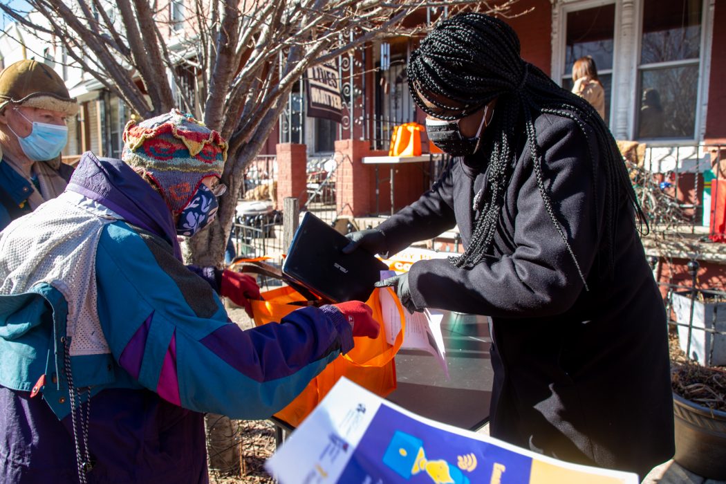 A woman is putting a laptop in an older woman's bag at an outdoor distribution event. All laptops given out at this event were distributed and refurbished through PHLDonateTech.