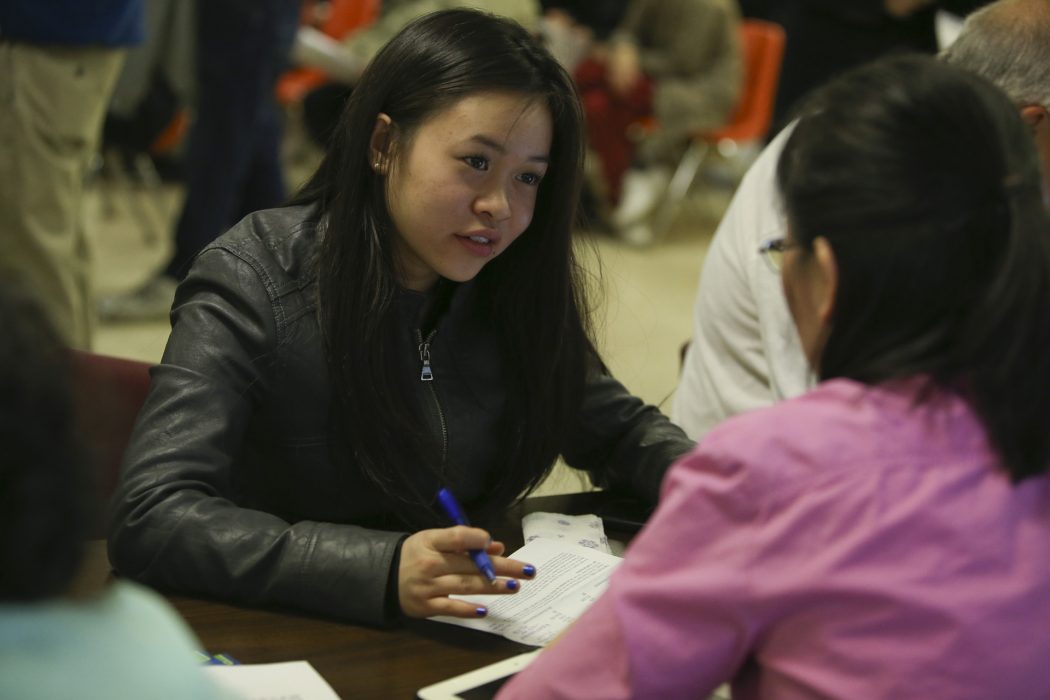 A woman is sitting down across from another woman and writing something down.