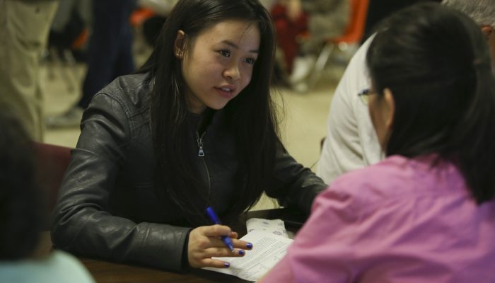 A woman is sitting down across from another woman and writing something down.