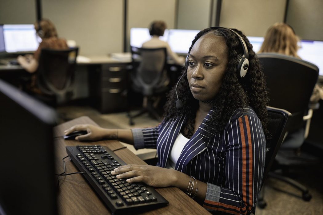 Woman in call center using headset and desktop computer.