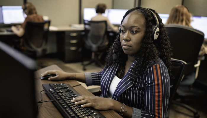 Woman in call center using headset and desktop computer.