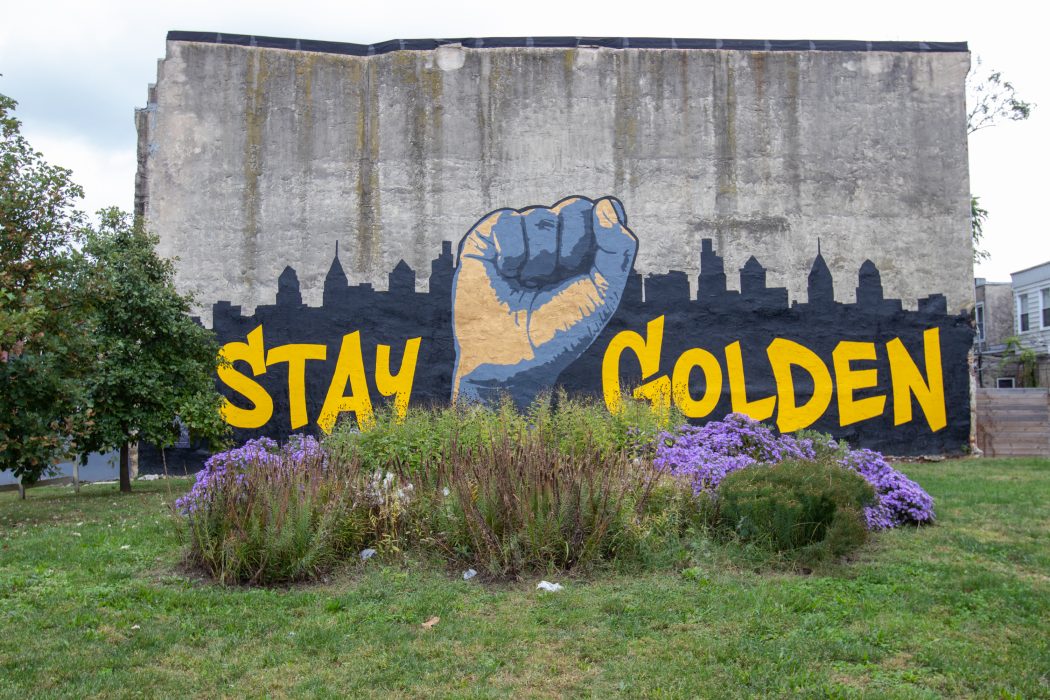 a mural of a raised fist in front of Philadelphia's skyline that says stay golden