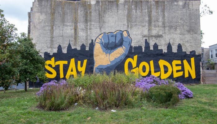 a mural of a raised fist in front of Philadelphia's skyline that says stay golden