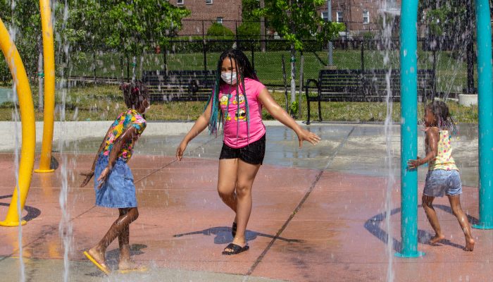 Three young girls play in the water at a sprayground.
