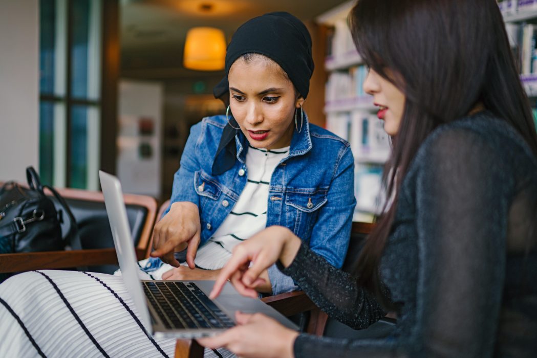 Two women pointing to information showing on a computer screen