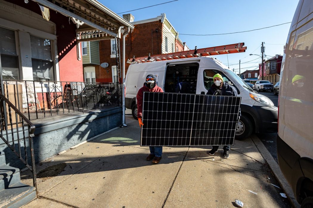 Two people carrying a solar panel to install on a house at a Solarize Philly event.