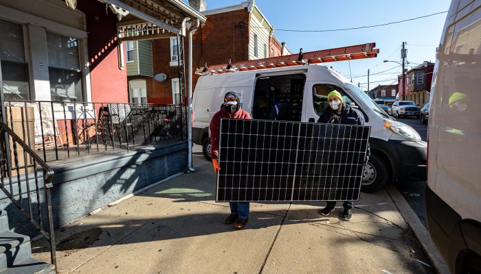 Two people carrying a solar panel to install on a house at a Solarize Philly event.