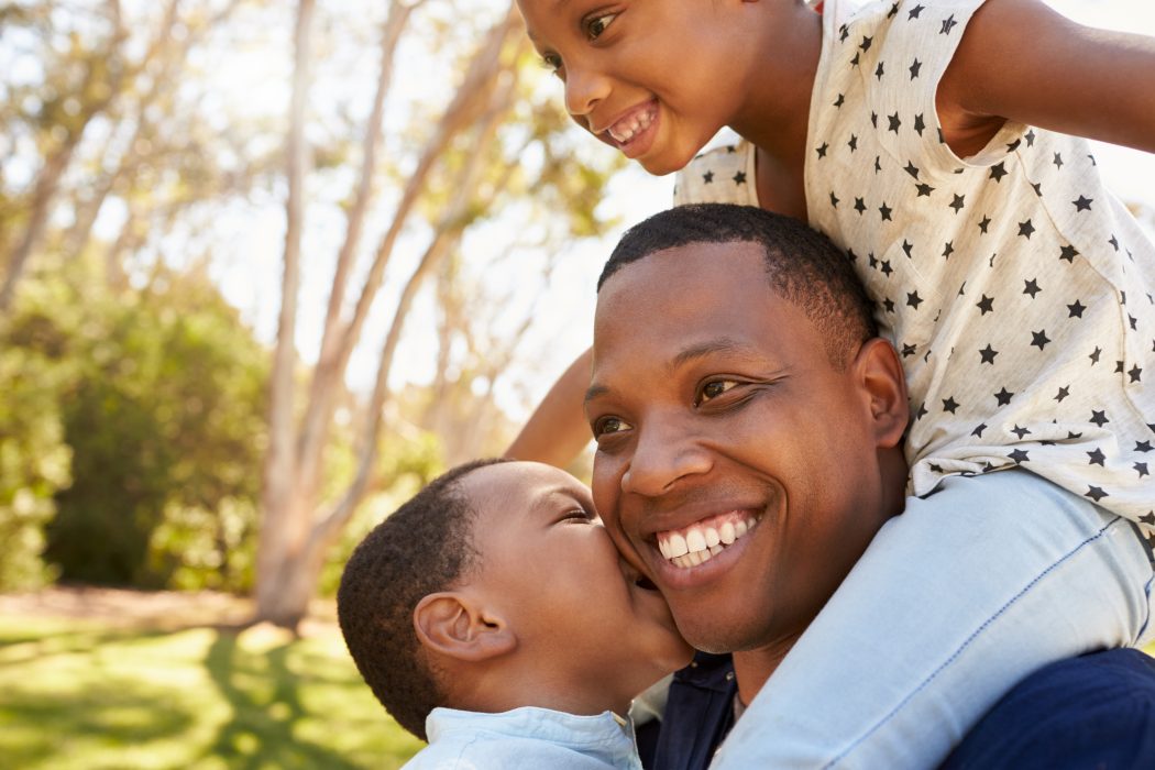 African American man carrying a child on his shoulders in a park