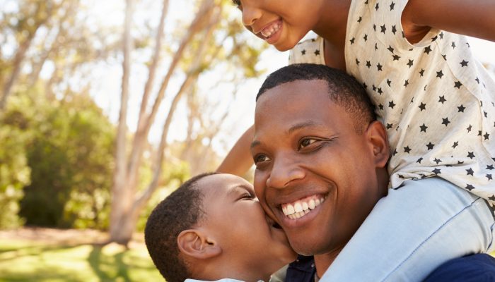 African American man carrying a child on his shoulders in a park