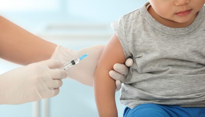 A medical professional holding the arm of a toddler and a syringe. The professional is about to inject the child.