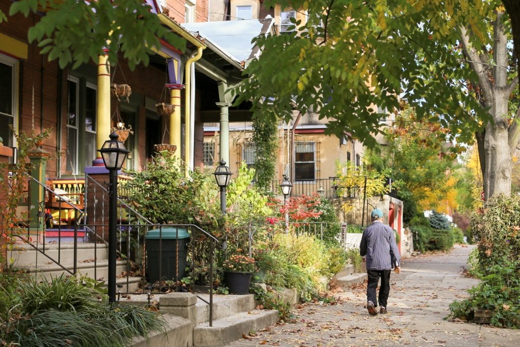 A man in a hat is walking on a sidewalk in Philadelphia. On the left is a house with a garden filled with greenery.