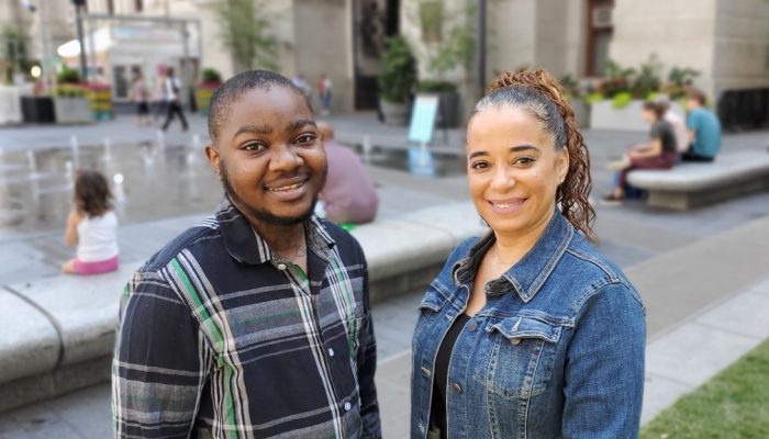 A young man and a woman pose in front of fountains in Dilworth Park