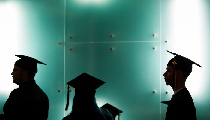 Graduates wearing cap in gown stand in a hallway